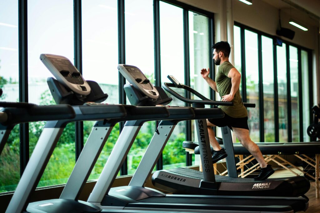 A man in athletic wear running on a treadmill at a modern gym with large windows